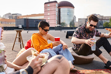attractive jolly friends in urban attires sitting on rooftop eating pizza and drinking cocktails