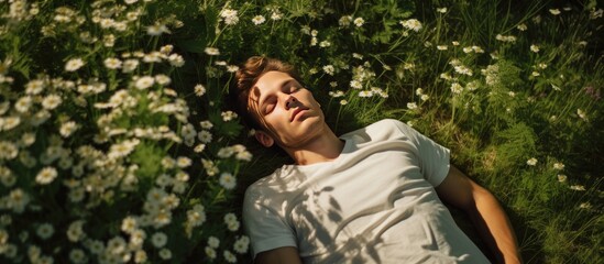 A young man is seen laying down in a field filled with colorful flowers, surrounded by green grass. He appears to be taking a break, possibly fatigued from work, taking advantage of the summer sun to