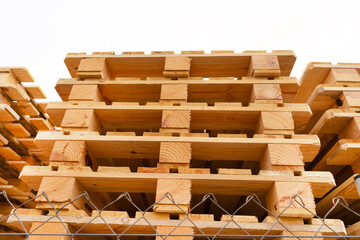 Pallets assembled from fresh sawn wood boards are stacked high on top of each other. Industrial production of pallets for transporting goods