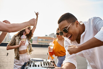 cheerful appealing diverse friends with sunglasses and cocktails partying on rooftop to DJ set
