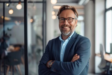 Fototapeta premium A man in a suit and glasses is smiling and posing for a picture. He is wearing a blue jacket and has his arms crossed. Concept of professionalism and confidence