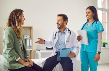 Smiling woman patient talking with man doctor and female friendly nurse holding report file with...