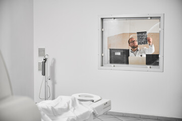 Medical computed tomography or MRI scanner. Doctor sitting at computer, examining MRI results. Male...
