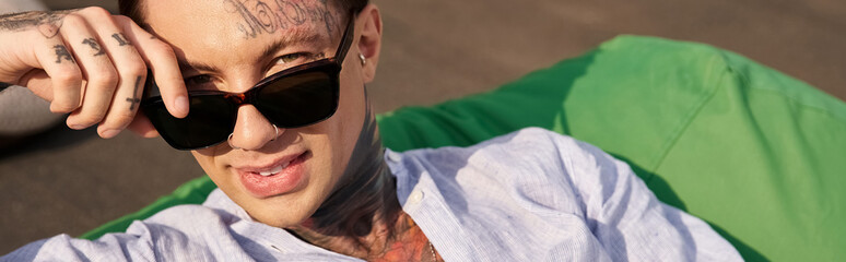 cheerful young man with tattoos and stylish sunglasses smiling at camera while on rooftop, banner - Powered by Adobe