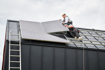 Installers connecting cables while installing photovoltaic solar panels on roof of house. Workers mounting of PV solar modules on rooftop. Concept of alternative and renewable energy.