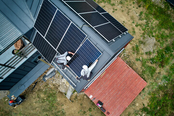 Installers building photovoltaic solar module station on roof of house. Men electricians in helmets...