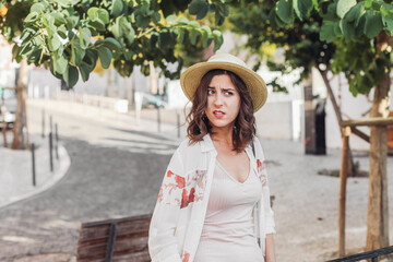 Young woman in a straw hat looks unsatisfied and surprised, walking on the streets of Lisbon 