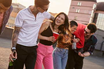 drunk cheerful multicultural friends in urban outfits holding alcohol drinks and having fun at party