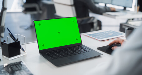Successful Caucasian Businessman Sitting at Desk Working on Green Screen Laptop Computer in Office. Anonymous Businessperson using Chroma Key Display. Stylish Bright Workplace. Over Shoulder Close Up.