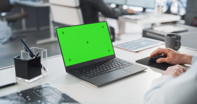 Successful Caucasian Businessman Sitting at Desk Working on Green Screen Laptop Computer in Office. Anonymous Businessperson using Chroma Key Display. Stylish Bright Workplace. Over Shoulder Close-up. - Powered by Adobe
