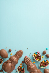 Fototapeta na wymiar Radiant Easter series concept. Top view vertical snapshot of chocolate eggs split open, spilling colorful candies, chocolate bunnies, sprinkles on pastel blue surface, with space for text or advert
