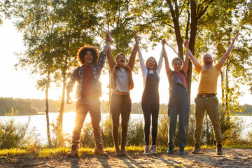 Euphoric group of five with raised hands celebrating in the glowing light of a lakeside sunset....