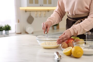 Woman whisking eggs in bowl at light marble table indoors, closeup. Space for text
