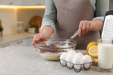 Woman making chocolate dough with whisk in bowl at gray marble table, closeup