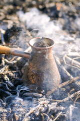Fototapeta premium Making coffee in cezve on the bonfire when camping or hiking in the nature. Coffee on campfire.