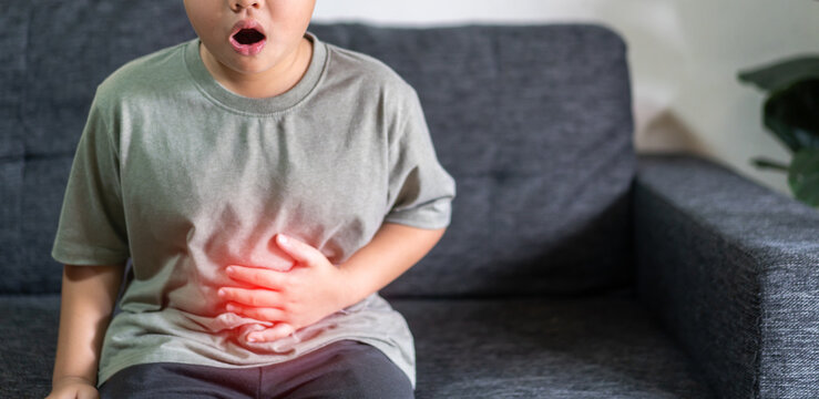 Portrait of sick unhappy little child asian boy touching belly stomach with suffering from stomach ache pain, gastritis, gastroenteritis, food poisoning, diarrhea, intestinal inflammation at home