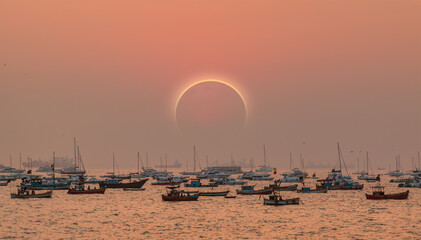 Solar eclipse - Colorful fishing boats near the shore of dirty water of Arabian sea at amazing sunrise - Mumbai, India