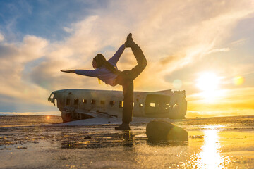 Woman on the Solheimasandur plane in Iceland performing a Natarajasana yoga pose to open the hip...