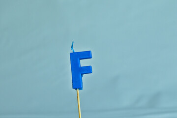 close up on a blue letter F birthday candle on a white background.
