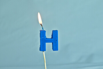 close up on a blue letter H birthday candle with fire on a white background.
