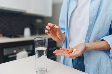 A woman holding a pill in front of a glass of water, with another glass of water in the background