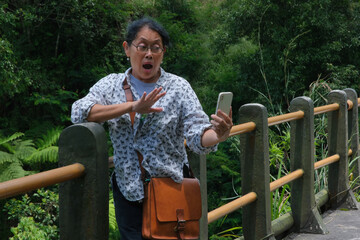 A woman is leaning against a bridge railing while holding a smartphone; surprised expression