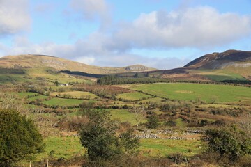 Landscape in rural County Sligo, Ireland in early springtime featuring rolling hills of green field farmland pastures bordered by hedges, trees and dry stone walls with mountain visible in background