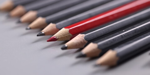 Closeup of one red wooden pencil among many black background. Distinctive personality traits concept