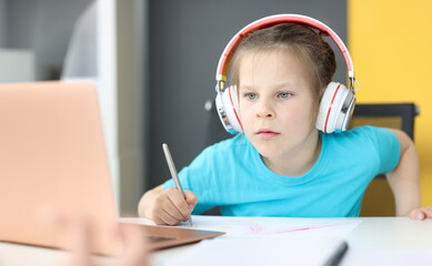 Little girl schoolgirl in headphones sitting in front of laptop at home. Homeschooling concept