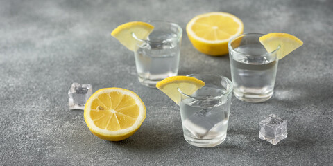 Cold vodka in a shot with ice and lemon, gray concrete background. Side view, selective focus, banner. - 755564004