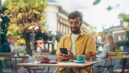 Handsome Multiethnic Man Sitting on a Terrace in a Cafe, Having a Cup of Coffee with Pastry. Happy Indian Man Connecting with Friends Online, Replying to Social Media Posts and Emails on a Smartphone