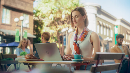 Female Freelancer Using Laptop Computer for Remote Online Work in a Cafe. Young Creative Woman Having Breakfast Croissant with Coffee while Teleworking From a Terrace on a Sunny Summer Day