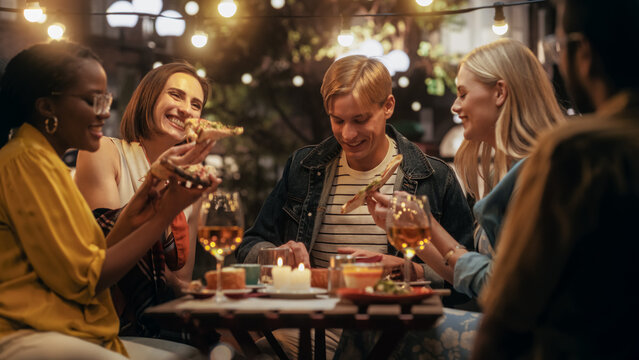 Young Multiethnic Friends Enjoying a Night Out in a Cafe. Eating Delicious Italian Pizza. Young Men and Women Having Fun Conversations on a Terrace, Enjoying Tasty Food and Beverages