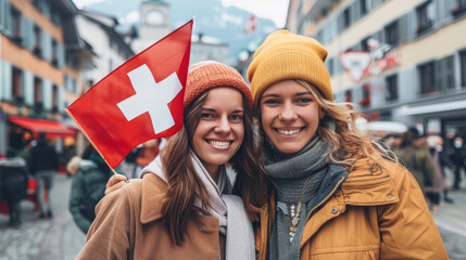 Two Swiss cheerful woman friends holding a Swiss flag on Switzerland city street - obrazy, fototapety, plakaty