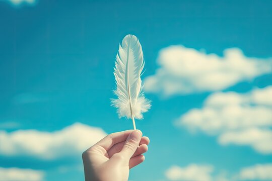 A hand holding a feather in the air with a blue sky in the background