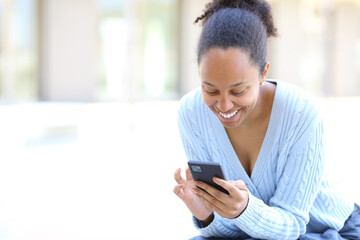 Happy black woman in the street checking cell phone