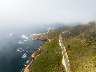 Aerial view of a coastal road passing through mountains in foggy weather