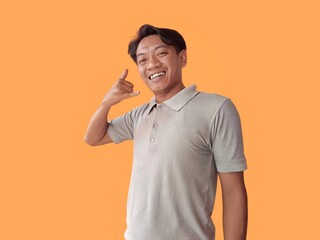 Handsome asian man standing over orange background smiling doing talking on the telephone gesture and pointing to you. call me.