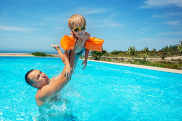 Dad lifting a child high above the water in swimming pool - 755579050