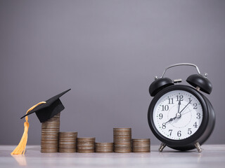 Black alarm clock, Graduation hat and stack of coins. The concept of saving money, manage time to...