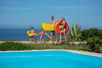 Family head to pool by sea, with floats full height portrait - 755580255