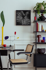 Workplace interior with mock up poster frame, black desk, rattan chair, stylish rack, books, yellow vase with leaves, modern sculpture, wall with stucco and personal accessories. Home decor. Template.
