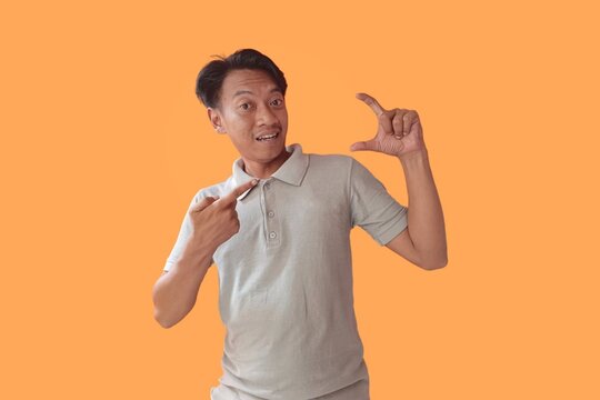 Handsome young man wearing gray t-shirt standing isolated over orange background, taking a selfie, pointing finger at camera