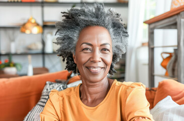Smiling middle aged mature grey haired woman sitting on her sofa in the living room at home. Senior woman posing on sofa looking at camera. Single mature senior in living room. 