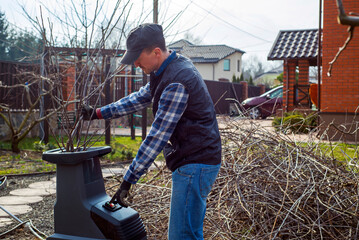 Male gardener using electric garden grinder to shred cut tree branches during spring cleaning. Cleanup around the house. Spring gardening. Pruning trees.