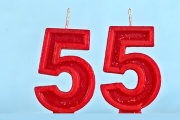 close up on a red number fifty fifth birthday candle on a white background.
