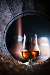 A glass of whiskey in old oak barrel. Copper alambic (distiller) on background. Traditional alcohol distillery concept - 755594014