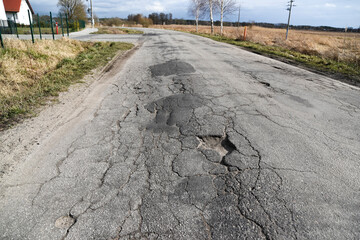 Potholes in the road, a dilapidated asphalt road with rainwater in the middle.