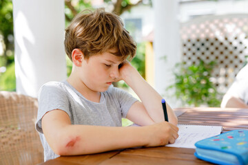Hard-working sad school kid boy making homework during quarantine time from corona pandemic...