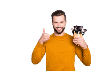 Portrait of attractive joyful visagist with bristle showing thumb up with finger having verity of brushes in arm, approve, advice, standing over grey background